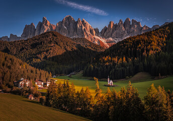 Val Di Funes, Dolomites, Italy - Autumn view of St. Johann Church (Chiesetta di San Giovanni in Ranui) at South Tyrol with the Italian Dolomites in warm sunset colors at background and blue sky