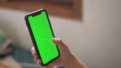 Hands of Asian woman holding checking touching scrolling smartphone green screen from bed room