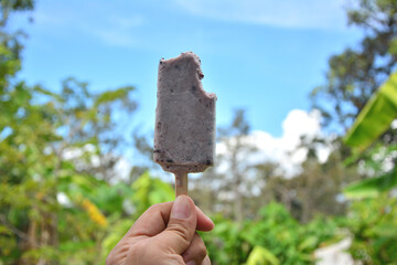 Ice cream in hand on tropical nature background.