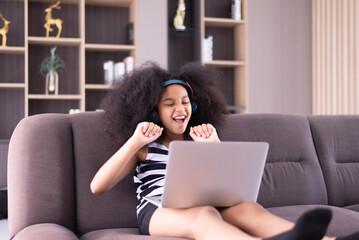 Happy young african girl listening to music on laptop and internet online