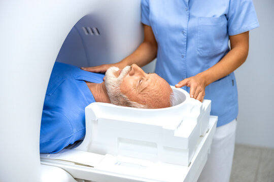 Female doctor assisting senior patient while doing MRI scan in medical examination room.