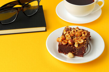 Piece of brownie cake with hazelnuts on yellow background