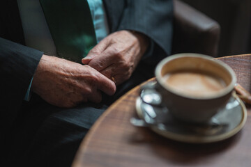 Fototapeta na wymiar hands of a old person wearing suit and drinking coffee in a cafe