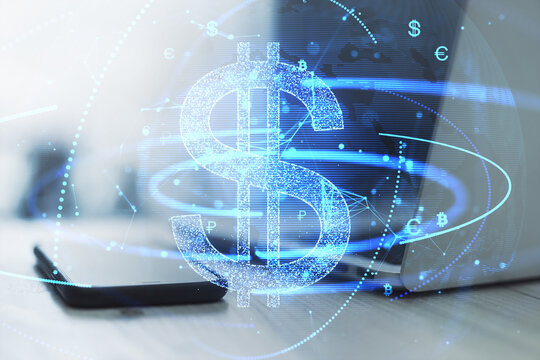 Close up of laptop computer and smartphone on desk with glowing digital blue dollar hologram on blurry background. Business finance and money exchange concept. Double exposure.