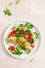 Omelette stuffed with tomato, broccoli, feta cheese and fresh green leaves of arugula and spinach. Healthy diet food, breakfast. Top view