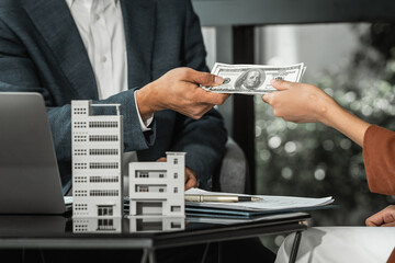 An Asian salesman offers to sell a house to an African customer. An Asian man, a real estate agent, shakes hands with a female African American client while purchasing an apartment.