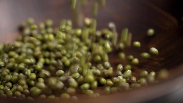 Dried mung beans falling into a dark wooden bowl for healthy dietary garnish cooking close up. Rotation