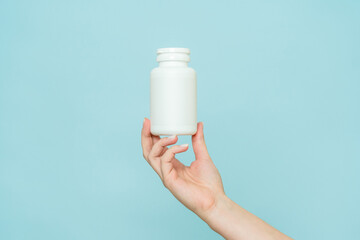 Woman's hand holds white plastic tube. Bottle for pill, capsule or supplement. Product branding...