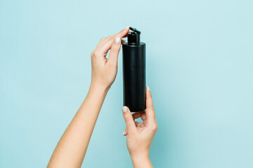 Hands hold black bottle of cosmetic product for skin on blue background