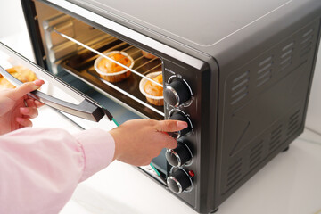 Woman's hands taking buscuit cupcakes out of mini oven