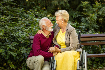 Senior man taking care of elderly woman in wheelchair and showing love and respect.
