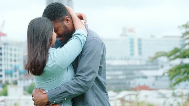 A handsome man and beautiful woman hugging each other in the park with a modern city in the background