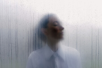 Woman behind wet foggy window. Loneliness concept