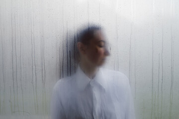 Woman behind wet foggy window. Loneliness concept - obrazy, fototapety, plakaty