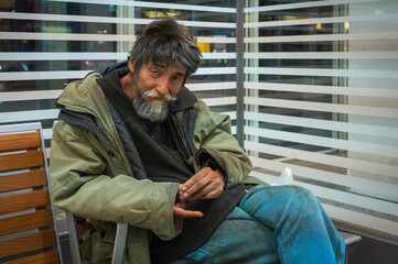 Ein obdachloser Mann sitzt und ruht sich aus - obrazy, fototapety, plakaty