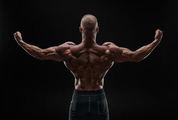 Naklejka premium Muscular man showing back muscles, isolated on black background. Strong male rear view