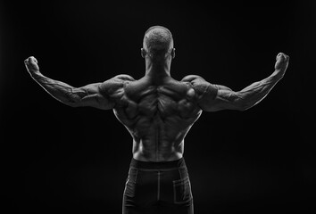 Silhouette of a strong bodybuilder. View from the back. Confident young fitness athlete with a powerful body and perfect abs. Black and white photography.