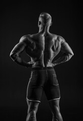 Fototapeta na wymiar Silhouette of a strong bodybuilder. View from the back. Confident young fitness athlete with a powerful body and perfect abs. Black and white photography.