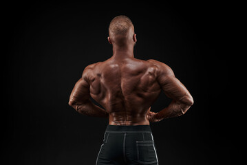 Fototapeta na wymiar Muscular man showing back muscles, isolated on black background. Strong male rear view