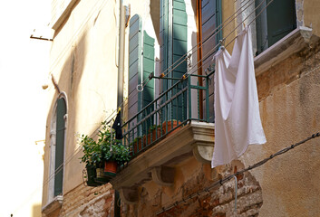 Fototapeta na wymiar The linen dried outside the windows - Venice, Italy. The wall with windows of the medieval house on the canal.