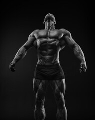 Fototapeta na wymiar Silhouette of a strong bodybuilder. Confident young fitness athlete with a powerful body and perfect abs. Black and white photography. Dramatic light.