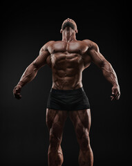 Muscular man shows his muscles against the background of a black wall. Bodybuilder, male naked torso, abs.