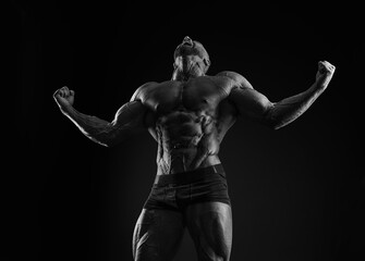 Fototapeta na wymiar Silhouette of a strong bodybuilder. Confident young fitness athlete with a powerful body and perfect abs. Black and white photography. Dramatic light.