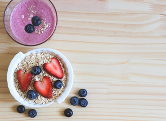 flat lay of  breakfast with a  glass of blueberry smoothie and oat or granola in white bowl, fresh blueberries, strawberries on wooden table. Healthy breakfast concept.