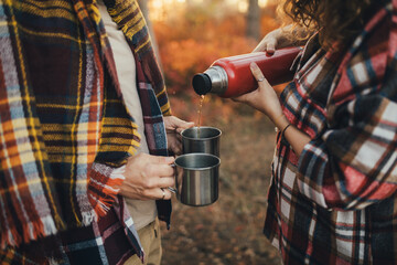 Happy couple drinking tea from thermos in an autumn forest.