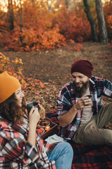 Happy couple drinking tea from thermos in an autumn forest.