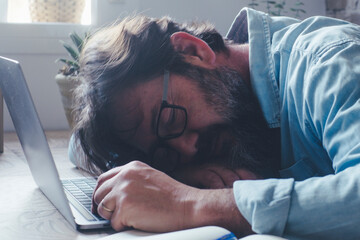 One man asleep on the laptop in home office workplace. Tired overwork people using computer and technology. Insomnia. Stress for work. Bored job business. Exhausted male indoor. Smart working problems - obrazy, fototapety, plakaty