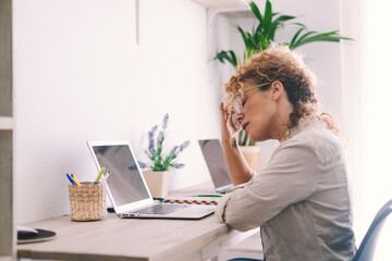 Tired woman touching neck and glasses in front of a. laptop in home office workplace. Small online...