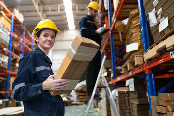 Caucasian businesswoman holding craft paper pack with buddy using clipboard checking wood Kraft stock in warehouse	