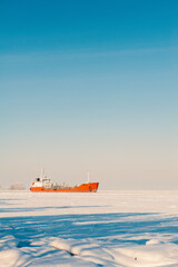 Fototapeta premium Winter shipping. Big cargo ship in frozen sea fairway