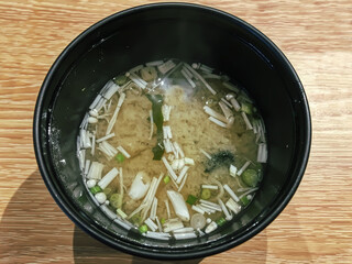 Japanese food Miso Soup in a black bowl on a wooden table.