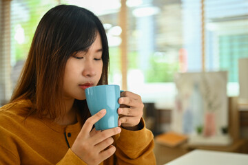 Pretty young Asian woman drinking hot tea in the morning at home