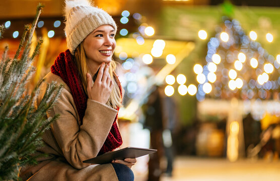 Portrait of happy beautiful young woman enjoying holiday and buy christmas tree on decorated market