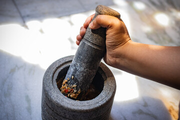 Mortar and pestle made of black rock being used by hand to crush or paste or grind spices like...