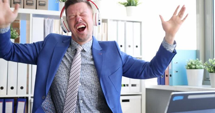 Young businessman happily dances in headphones in front of tablet monitor. Successful business broker concept