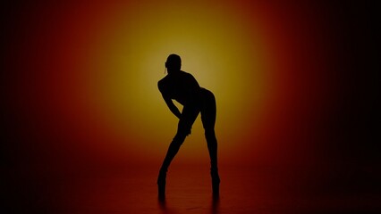 Woman dancer silhouette in high heels standing in the studio in yellow spotlight. Isolated on...