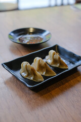 3 pieces of grilled gyoza in a black ceramic plate served with chili soy sauce