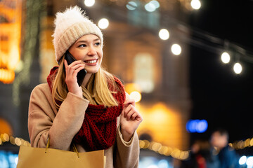 Portrait of smiling woman using mobile phone in the city at winter. People communication concept - obrazy, fototapety, plakaty