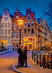 Fototapeta premium Amsterdam canals in the evening during Christmas, a couple of men and women on a city trip in Amsterdam in the Netherlands during winter. old city street with street lanterns in the evening