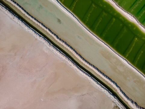 Aerial view of a salt mine with different hues of green and salt dividers running diagonally through the image, Western Australia. Top down perspective.