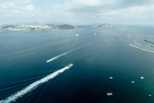 Aerial view of ferries and sailboats crossing the Gulf of Naples from Procida Island to Naples, view of Monte di Procida and Faro Capo Miseno promontory, Naples, Campania, Italy.