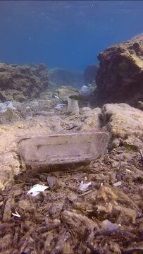 Vertical video, Camera moving forwards low along seabed covered with lots of plastic debris in crevice between rocks. Seafloor covered with wery many plastic garbage polluting Mediterranean Sea