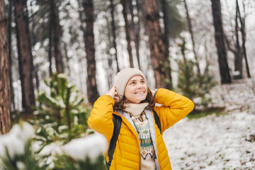 Young adult caucasian woman in a hat and yellow jacket walking n the winter forest breathing fresh air