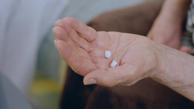 In front of the camera capturing video of a old hand holding two medical pills in hands after she take from the bottle