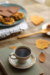 Cup of tea or coffee, plate with desserts, dried oranges, bowl of grapes, scented candles, vintage books, pumpkins and autumn leaves on the table. Autumnal hygge. Selective focus.