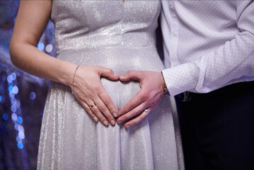 Hands on pregnant mom's belly at heart figure. Family waiting for baby birth during pregnancy